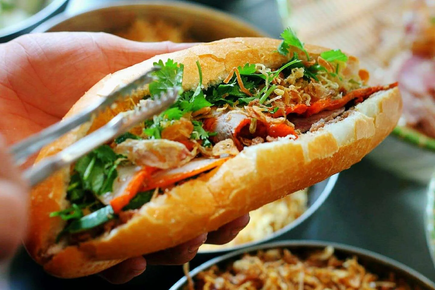 A bánh mì filled with meat, herbs and vegetables, held in one hand