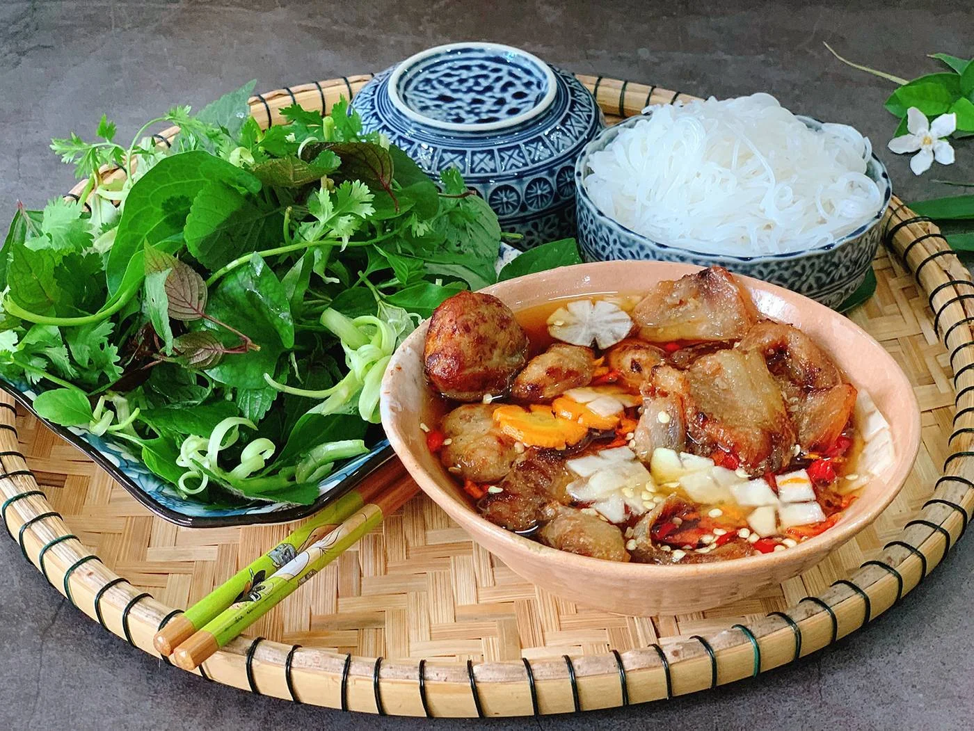 Bún chả with grilled pork, rice noodles and fresh herbs on a bamboo tray