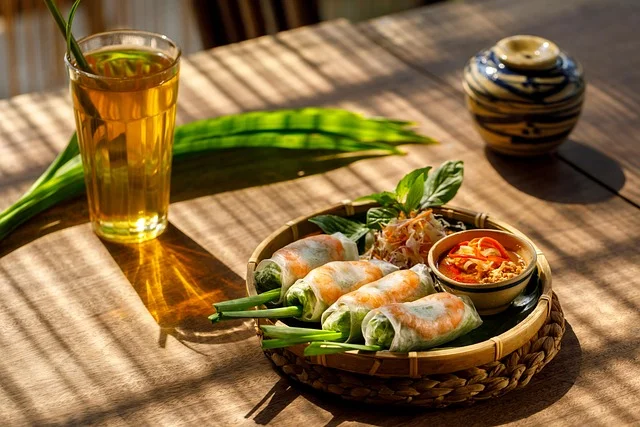 Fresh spring rolls and dipping sauce on a sunlit wooden table beside tea